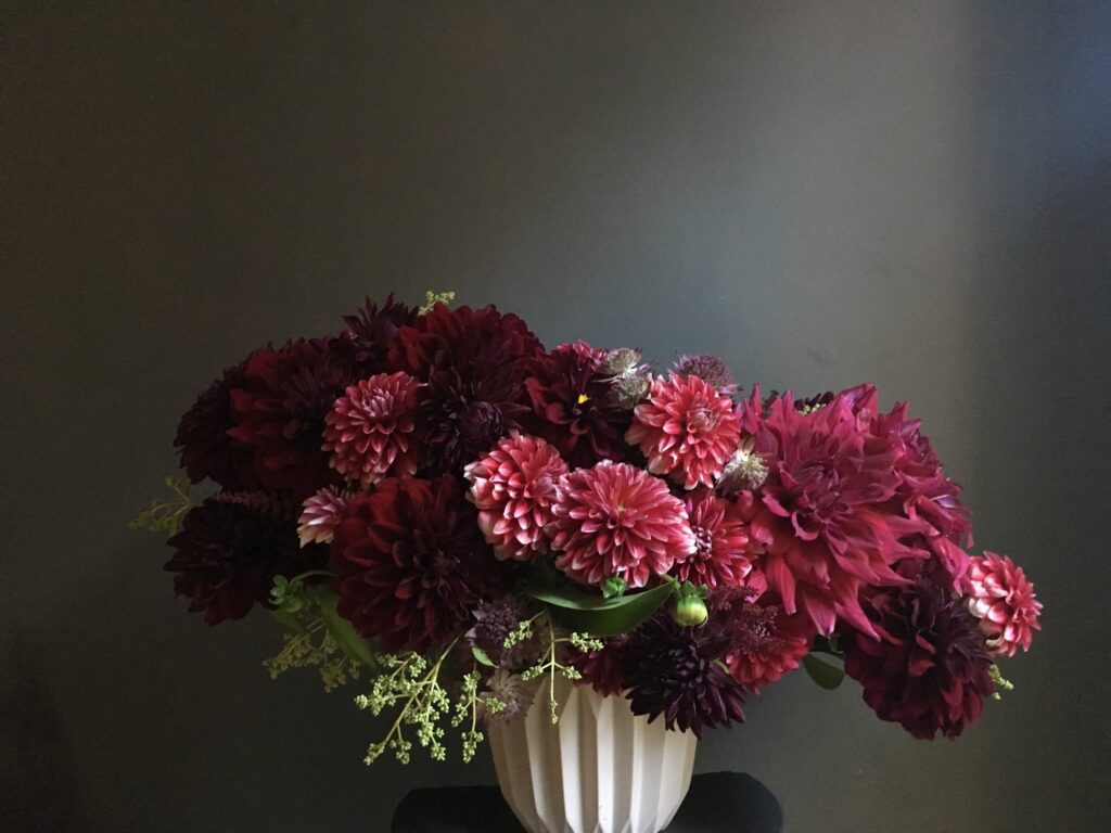 Amorous Floral design. A lush bouquet of deep red and burgundy flowers in a white vase against a dark background, illustrating an air of elegance and romance.