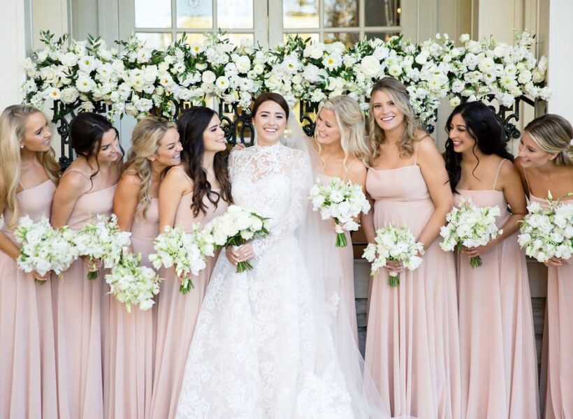 Bride in white gown with bridesmaids in blush dresses holding white flower bouquets.