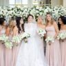 Bride in white gown with bridesmaids in blush dresses holding white flower bouquets.